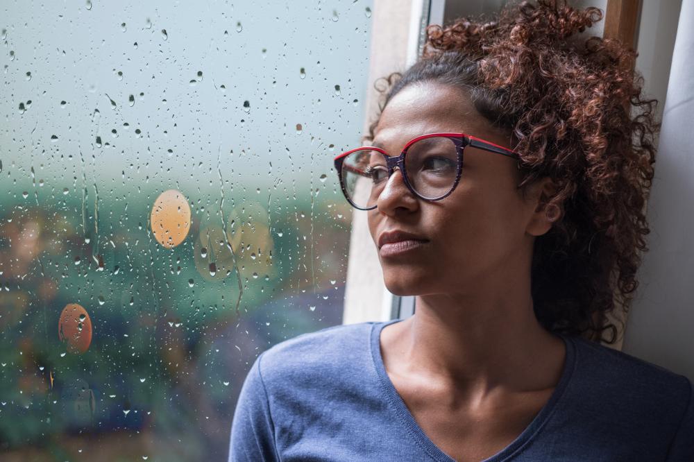 Click to enlarge Woman stares out the rainy window, contemplating contacting a pain and suffering lawyer. 
